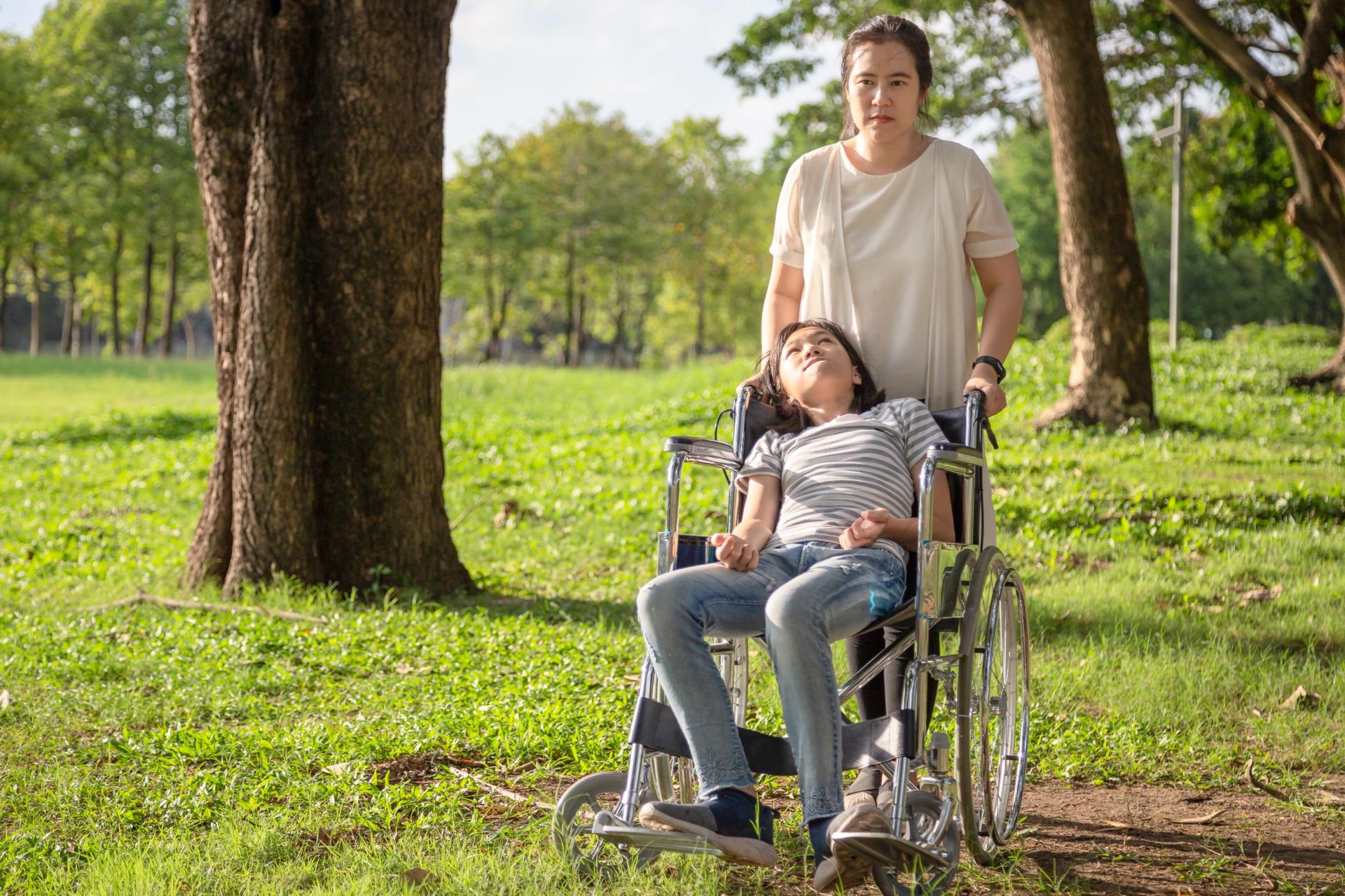 Carer helping little girl on wheelchair out in the woods