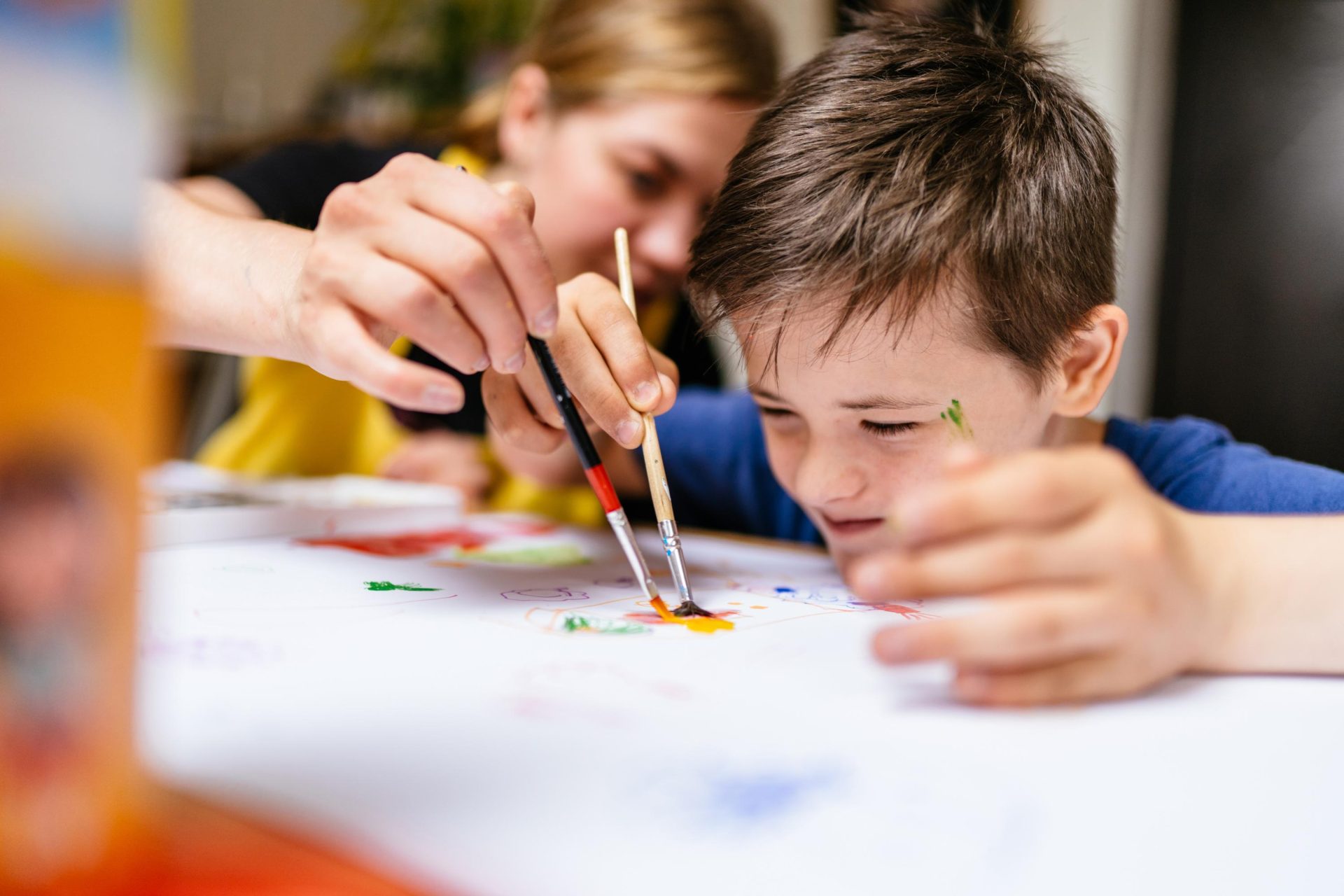 Child who needs tailored assistance being helped to paint by carer